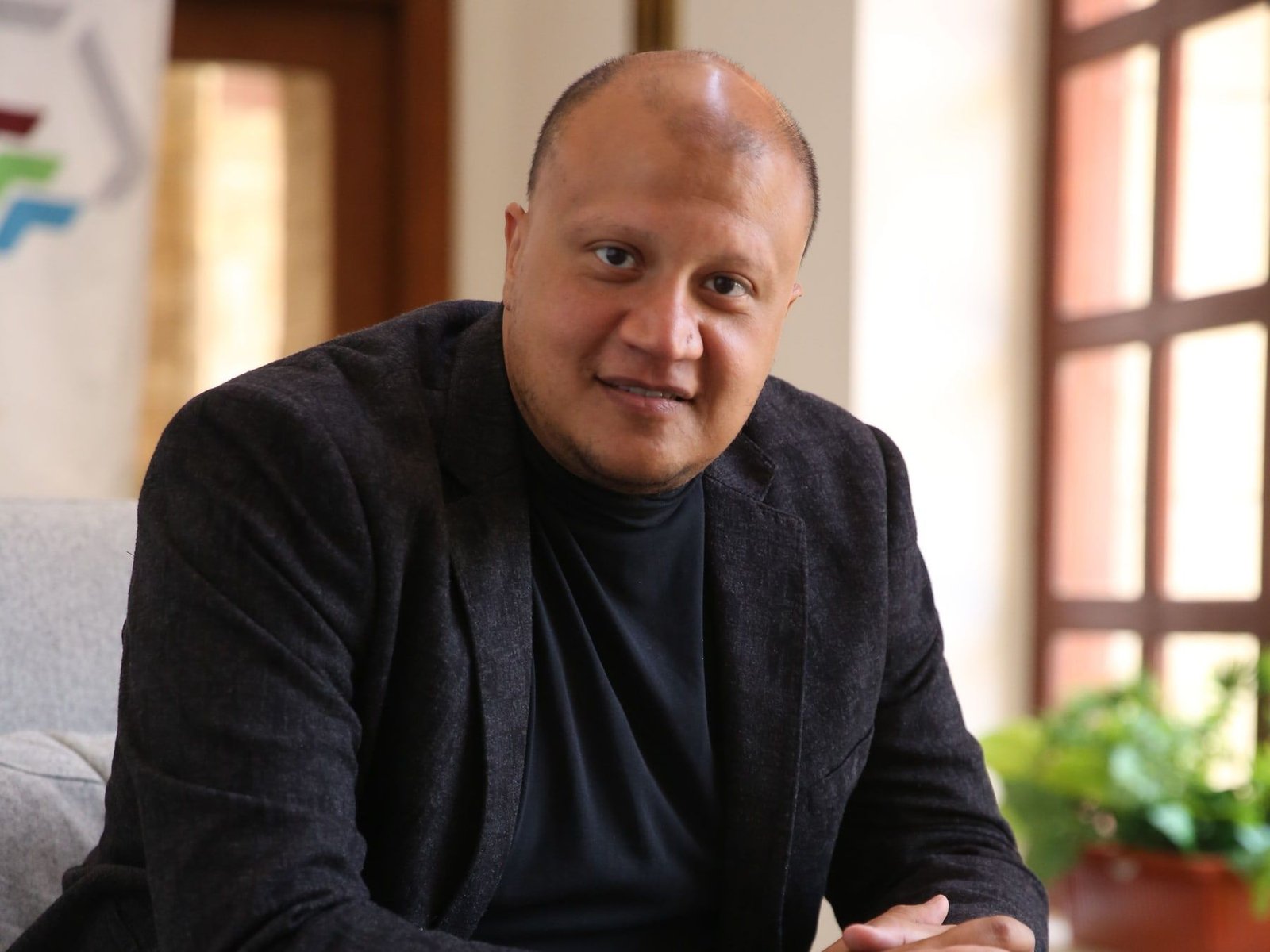 محمد الشريف جالسًا في حديث، ويداه متشابكتان، على مقعد بجوار نافذة.